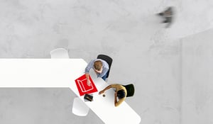 Zwei Personen sitzen an einem weißen Tisch, arbeiten gemeinsam an Dokumenten und besprechen Inhalte.