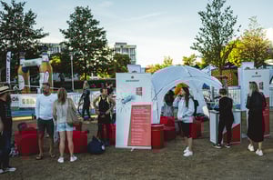 Besucherinnen und Besucher im Chill-out-Bereich des DATAGROUP Triathlon Nürnberg mit Infostand, Sitzsäcken und Sonnenschirm.