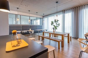 Gemütlicher Ess- und Aufenthaltsbereich bei DATAGROUP Mainz mit langen Holztischen, Bänken und großer Fensterfront mit Vorhängen.