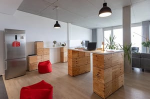 Gemeinschaftsküche im DATAGROUP Büro Mainz mit Holz-Stehtischen aus Kistenmodulen, roten Sitzsäcken und moderner Ausstattung.