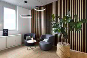 Einladende Lounge-Ecke im DATAGROUP Büro Mainz mit zwei Sesseln, kleinem Tisch, großer Pflanze und Wand in Holzlamellen-Optik.