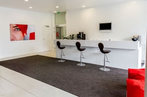 Empfangsbereich im DATAGROUP Büro Ulm mit modernem weißen Tresen, Barhockern und Wandbild in der Markenfarbe Rot.