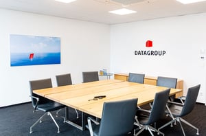 Moderner Konferenzraum bei DATAGROUP Ulm mit großem Holztisch, schwarzen Stühlen und Unternehmenslogo an der Wand.