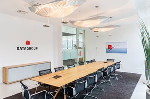 Moderner Konferenzraum im DATAGROUP Büro Ulm mit großem Holztisch, schwarzen Stühlen und stilvoller Deckenbeleuchtung.