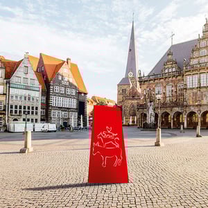 Bremer Marktplatz mit historischen Fachwerkhäusern, gotischem Rathaus und einer stilisierten roten Silhouette der Bremer Stadtmusikanten auf gepflastertem Platz bei goldenem Sonnenlicht