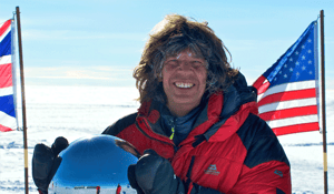 Photo of Michael Martin - photographer, graduate geographer and author of over 30 books - in a red snowsuit in a snowy landscape in front of US and British flags.
