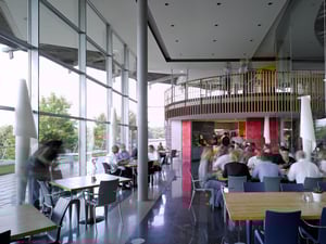 Moderne Kantine im DATAGROUP Hauptsitz Pliezhausen mit großen Glasfronten, runden Balkonen und Mitarbeitenden beim Mittagessen.