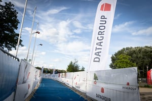 Blick auf die blaue Zielgerade des Triathlons Nürnberg 2025 mit DATAGROUP-Bandenwerbung und Fahnen – Teilnehmer nähern sich dem Ziel.