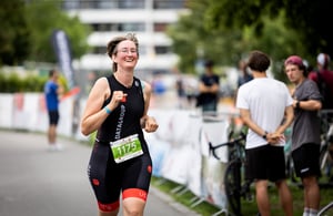 Eine Teilnehmerin im DATAGROUP-Triathlonanzug läuft lachend beim Triathlon Nürnberg 2025 durch die Strecke – sie trägt die Startnummer 1175.